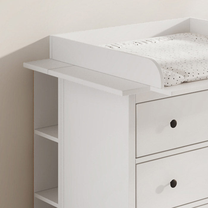 Seitliche Ansicht von einer weißen IKEA Hemnes Kommode, die durch Wickelaufsatz und Stauraumregal zu einer Wickelkommode umfunktioniert wurde. Auf dem Wickelaufsatz liegt zudem eine gepunktete Wickelauflage.