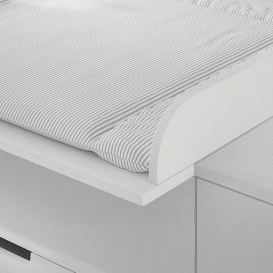 Detailansicht der vorderen Ecke einer weißen Wickelunterlage mit grauen Streifen, wie sie in einem dafür passenden Aufsatz auf einer Kommode liegt.