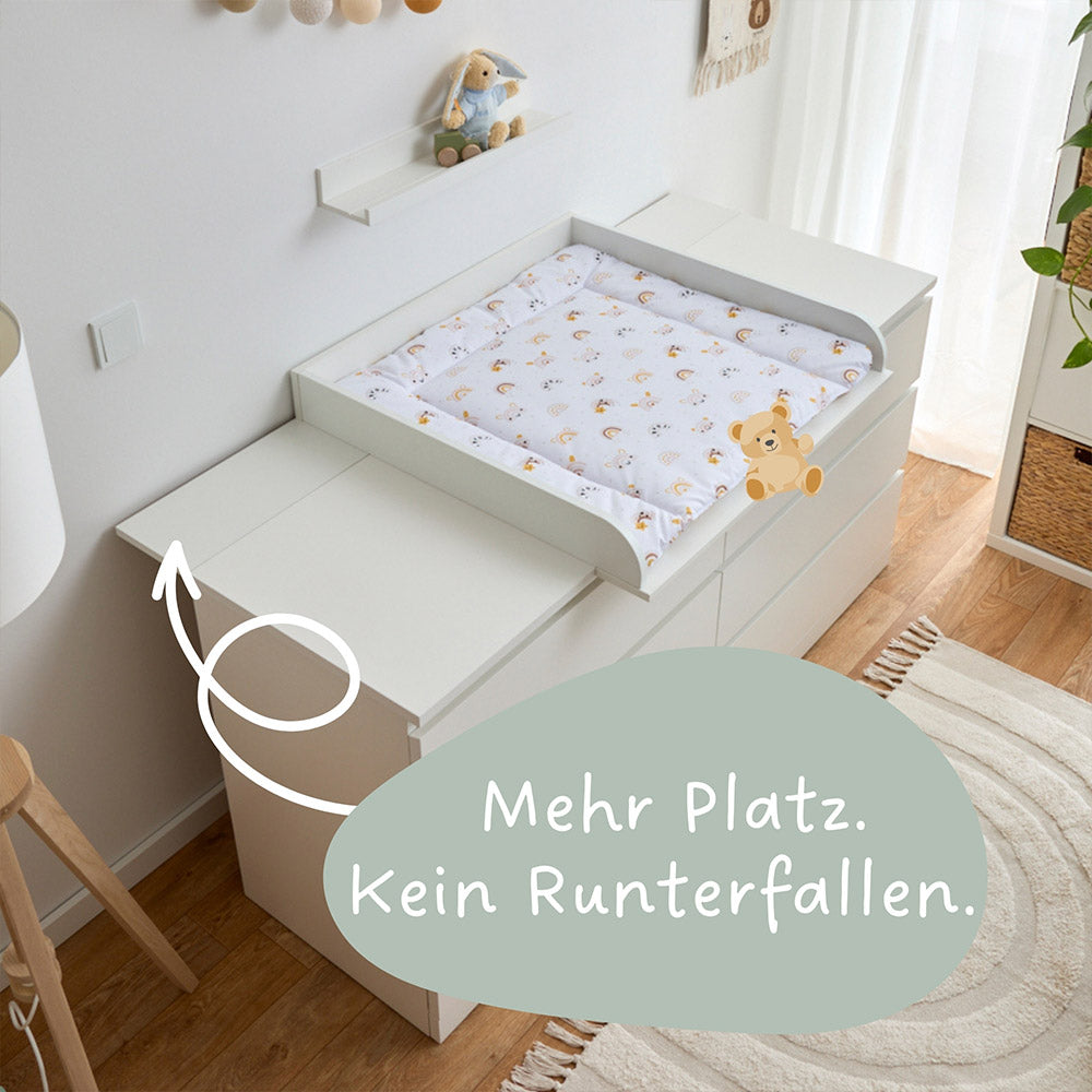 Eine IKEA Malm Kommode, mit 6 Schubladen, auf der sich ein weißer Wickelaufsatz und eine passgenaue Wickelauflage mit Regenbogenmuster befindet.