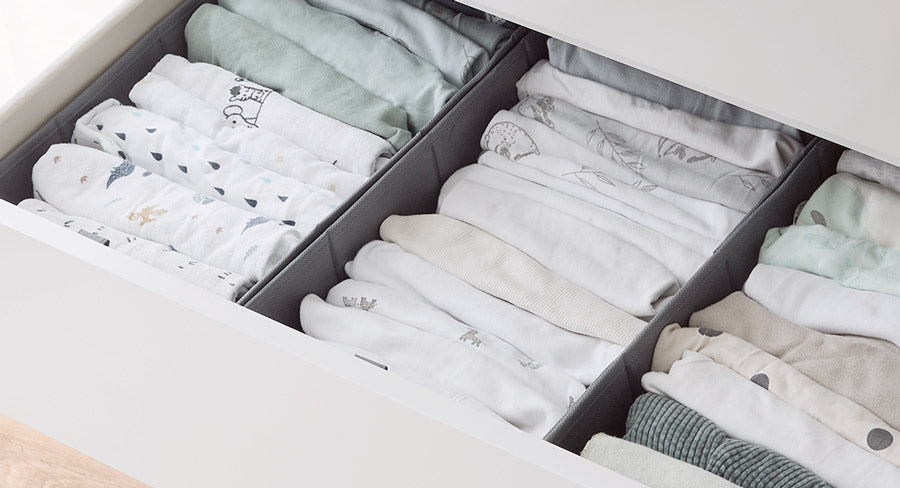 Mit Babykleidung gefüllte Organizer in einer Kommodenschublade.