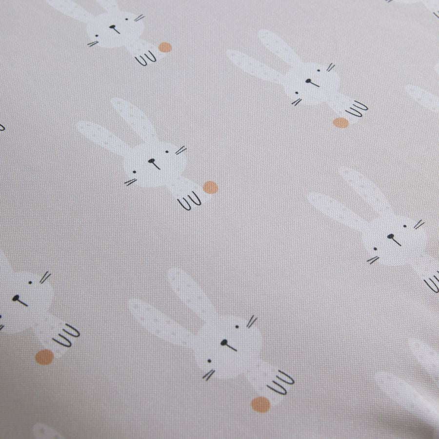 Zoom-Ausschnitt eines beigefarbenen Bezugs einer Wickelauflage, auf dem weiße Hasen zu sehen ist.