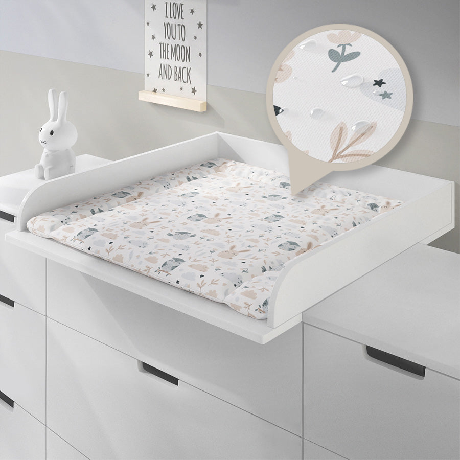 Weiße Wickelauflage mit Eulen und Hasen in einem 80 cm breiten Wickelaufsatz auf einer Ikea Kommode liegend. Ein kreisförmiges Detail zeigt eine Nahaufnahme der Wickelauflage mit Wassertropfen als wasserfestes Symbol.