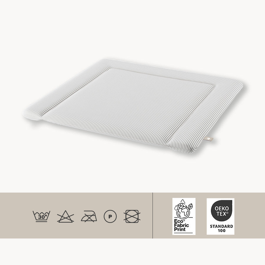 Freigestellte weiße Wickelauflage mit grauen Streifen und Pflegehinweisen, die sich auf die Art der Reinigung und Zertifizierungen, wie z. B. Öko-Tex beziehen.