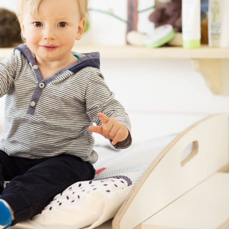 Kleinkind sitzend auf weißem Wickelaufsatz mit runden Seitenteilen aus finnischem Birkensperrholz